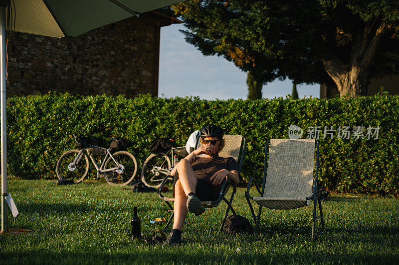 一个年轻人坐在后院的草坪椅子上喝着葡萄酒
