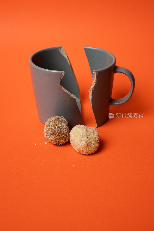 破碎的咖啡杯，上面有饼干，背景是鲜艳的橙色