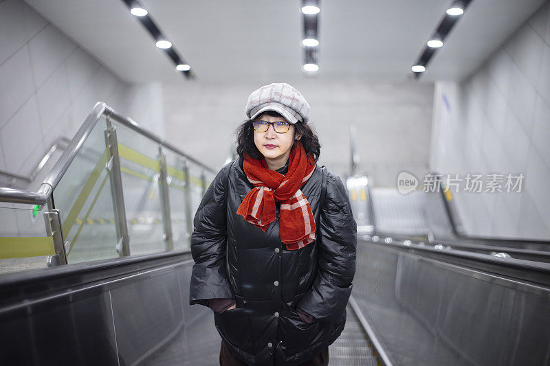 一位东亚妇女站在自动扶梯上，抬头看着镜头