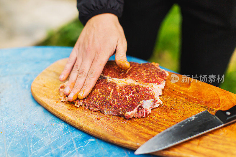 新鲜牛排。满足户外经验。晚餐在后院。木板上红肉。准备食物的过程。小牛肉。美味的小吃。户外用餐。盐和调味食品