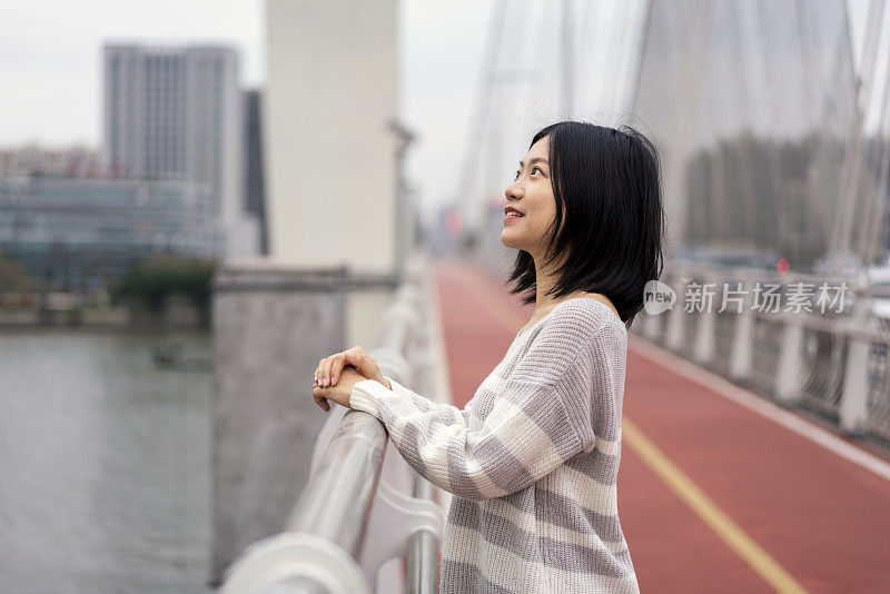 在市中心的一座桥上，一位亚洲妇女望着远方