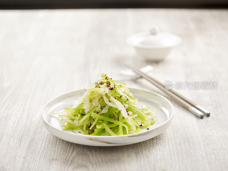 冷藏海蜇，芦笋，葱油生菜，用筷子夹在盘子里，灰色背景，侧视图