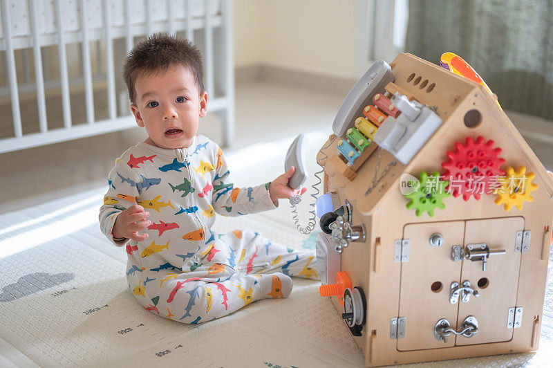 小男孩坐在家里地板上的婴儿安全软游戏垫上，在卧室里玩大型活动盒。10个月大的婴儿在家里玩耍