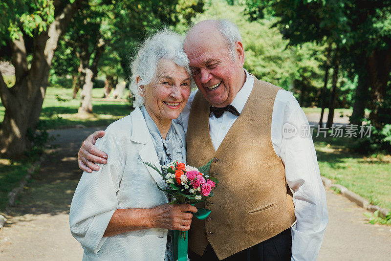 一对老夫妇在绿色的公园里散步。祖母和祖父在他们的金婚纪念日上。50年老人在一起的爱情故事。爷爷奶奶笑了。