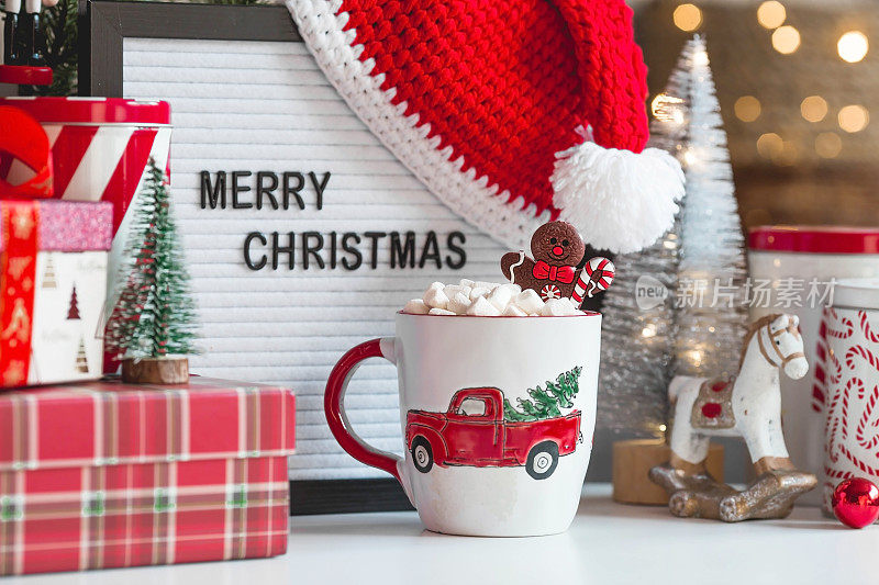 一个标牌上写着圣诞快乐，礼物，圣诞老人帽子，一杯热可可，棉花糖和姜饼人的背景是一个美丽的bokeh。温馨的新年和寒假概念