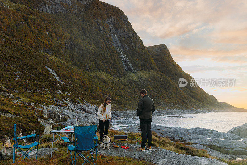 在挪威，女人和男人在海边野餐，欣赏日落时分的山景