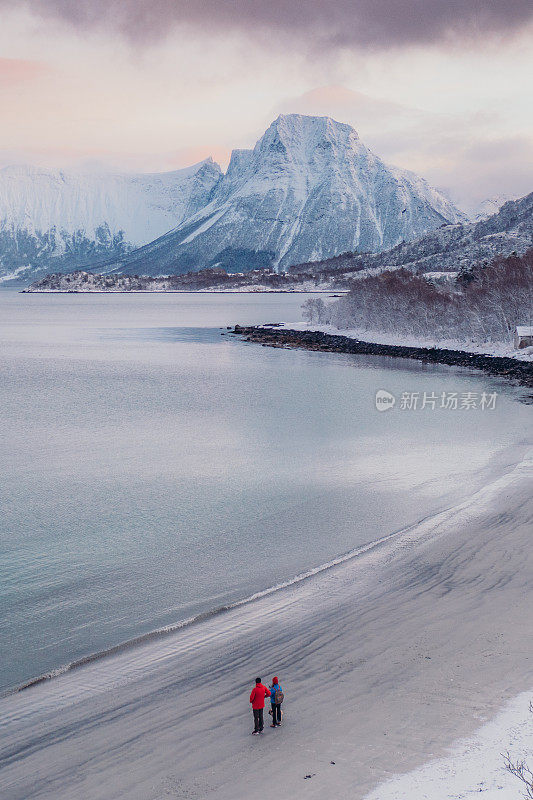 航拍图像的女人和男人走在风景秀丽的turqouse海滩在雪与山景在挪威