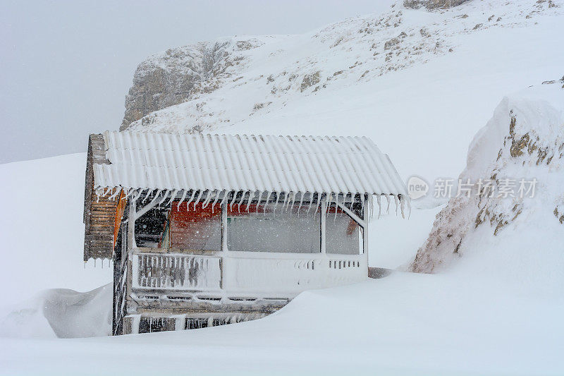 山上冰冻的木制滑雪小屋。山间小屋，小木屋，屋顶有冰柱的避难小屋。白雪覆盖的老木屋孤独地伫立在遥远的冬雪山间