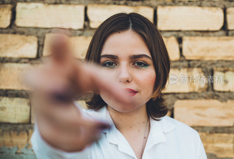 有吸引力的年轻女子在白衬衫的肖像，试图握住相机与手，砖墙背景。