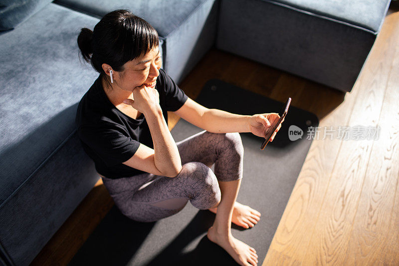 年轻的日本女子在家里锻炼后使用智能手机