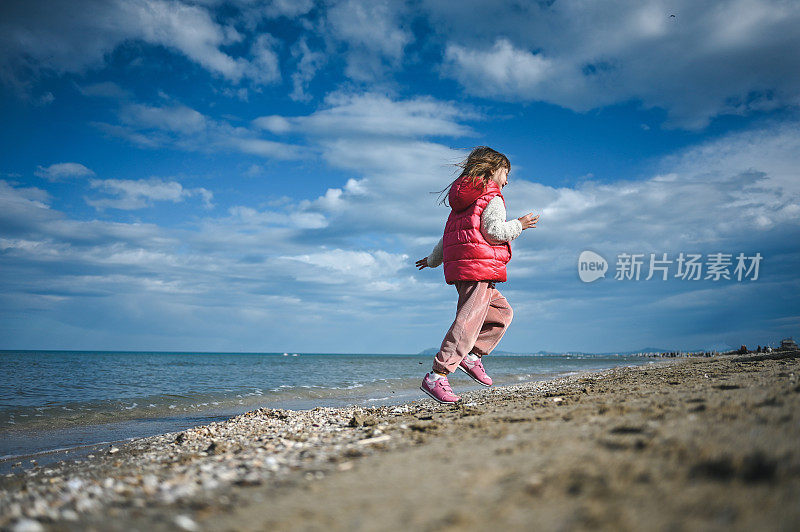 一个小女孩在沙滩上跳跃的背影。低角度视图。