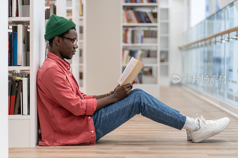 有书的非裔美国学生在图书馆消磨空闲时间，享受阅读。