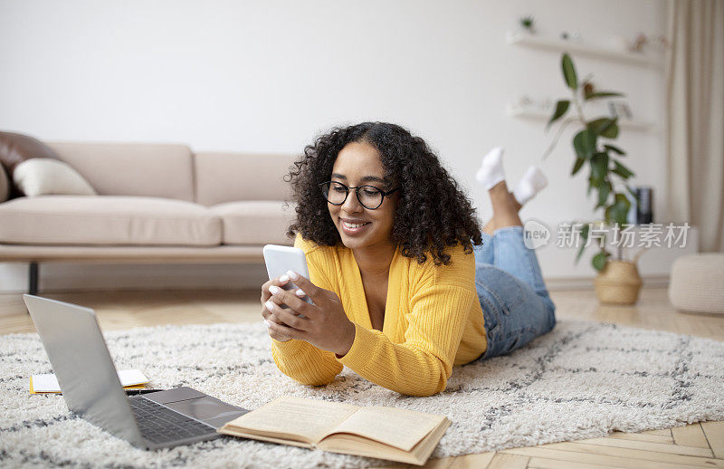 积极的年轻黑人女性使用笔记本电脑和智能手机进行远程工作，从家里在线交流，全程