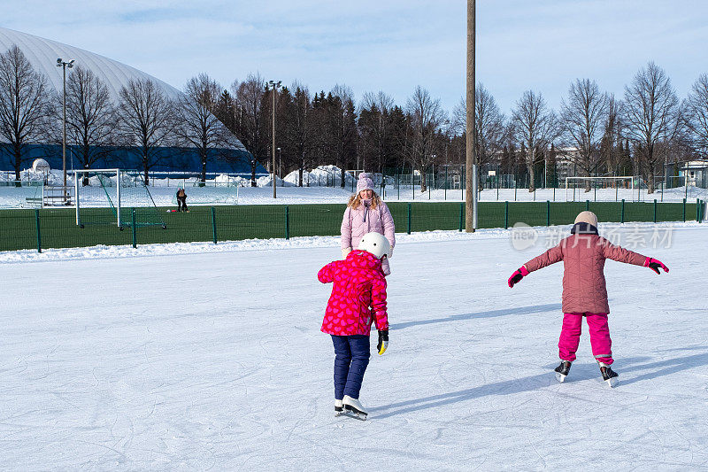 两个白人女孩，7岁，正在训练滑冰。一位妇女训练孩子们正确地站在冰鞋上。