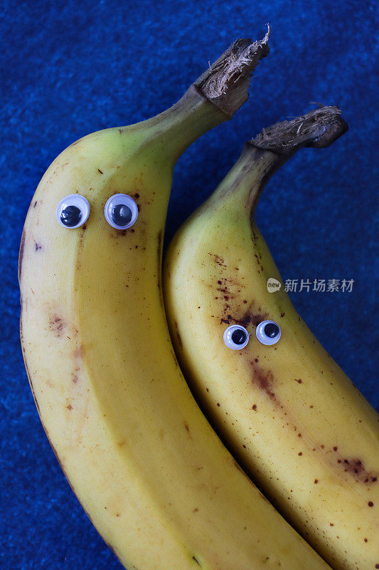 形象中有两个有趣的卡通人物，用成熟的香蕉做成，有着大大的眼睛，蓝色的背景，儿童健康饮食，幽默的概念