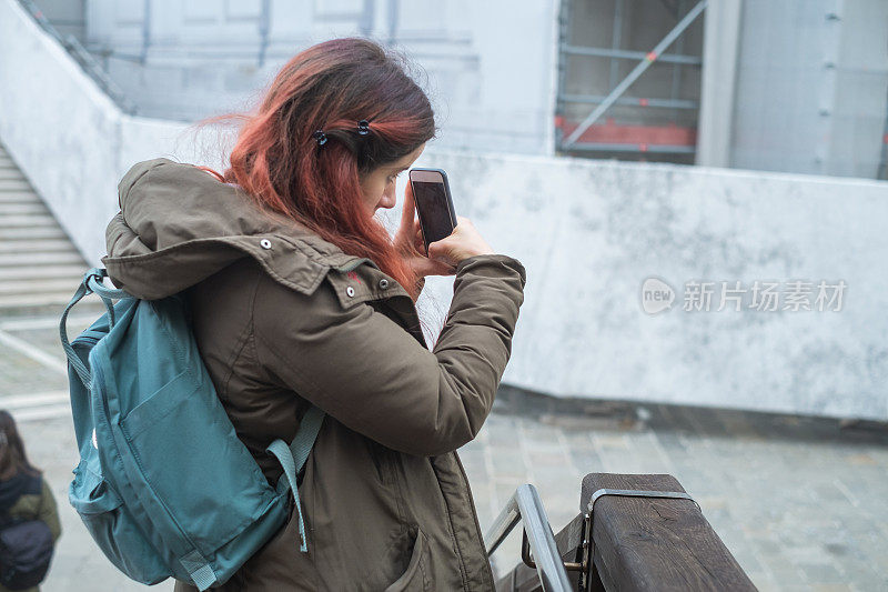 一名年轻女子在意大利威尼斯的一座人行天桥上用智能手机拍照