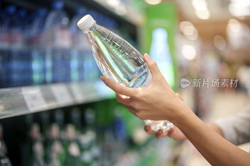 特写女人的手，一个女人从杂货店的架子上挑选一瓶水