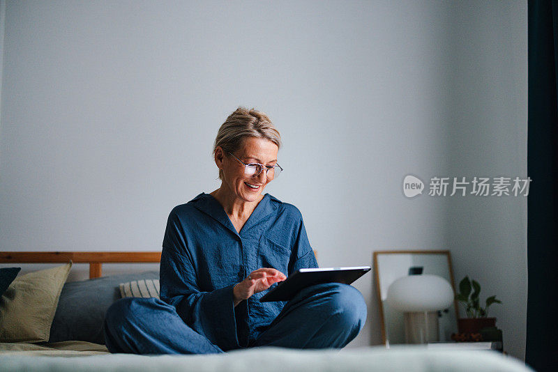 一位美丽的老妇人坐在床上使用数码平板电脑的肖像