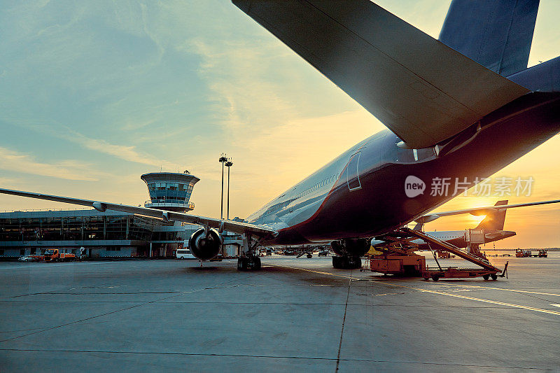 现代客机在机场的空侧停机坪停在航站楼门口，近距离观察飞机部件，喷气发动机，机翼，窗户，齿轮，牵引车，正午的阳光视野