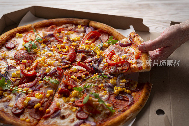 白种人的手从白色木桌上的纸盒里取出一片大披萨