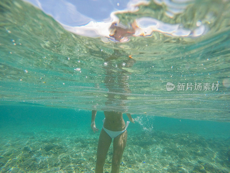 水下拍摄的年轻女子站在热带清澈的海水中度假的人的概念