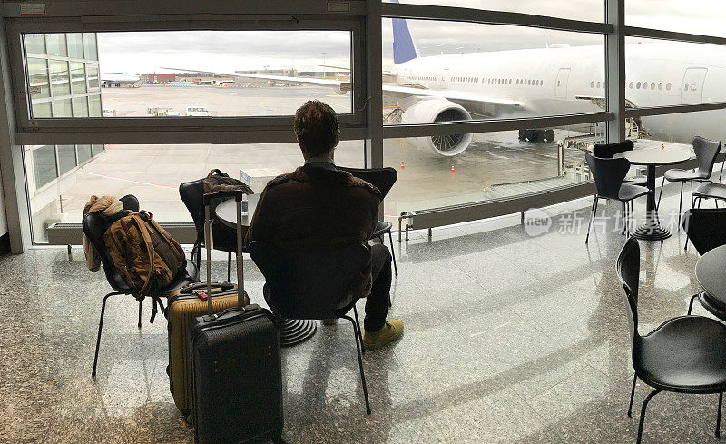 一名男子与行李一起坐在机场门口;飞机外部窗