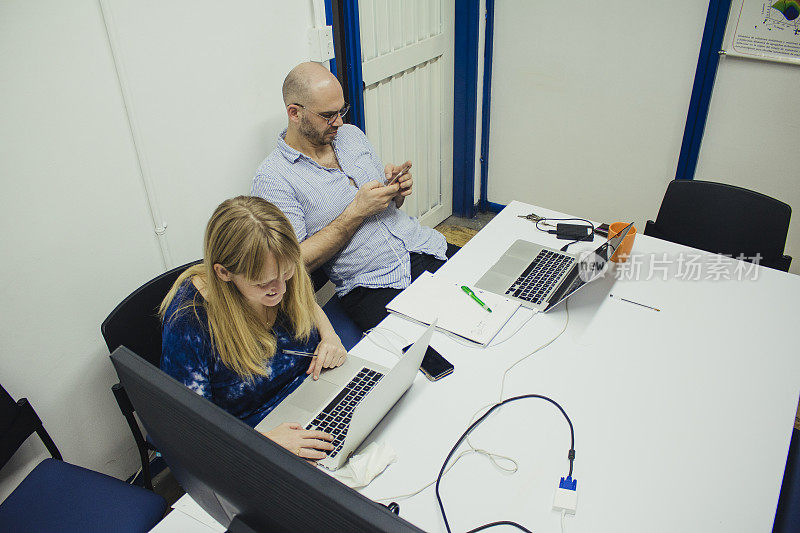 临时办公室里的两位专业同事，一边使用智能手机和笔记本电脑，一边表达积极情绪