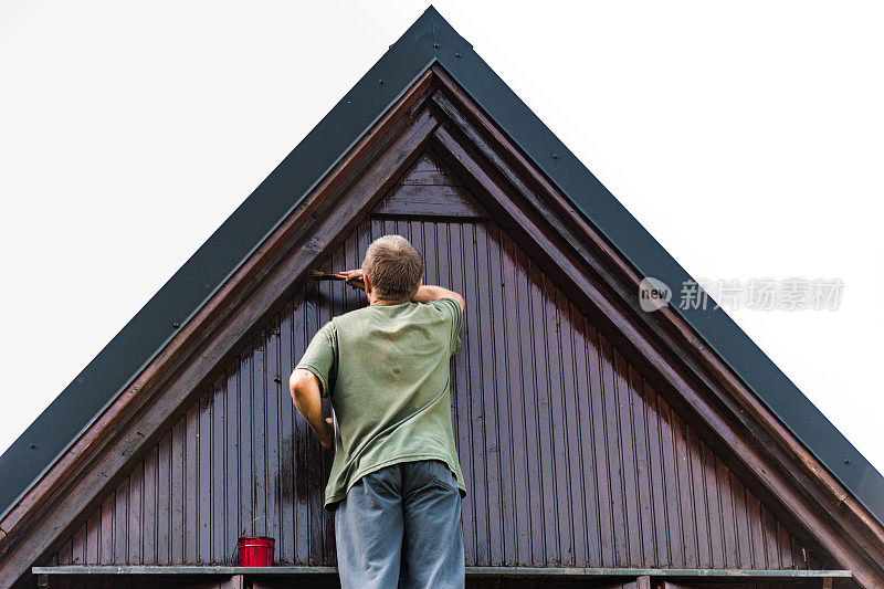 一名成年男子正在粉刷和翻修一处小屋的屋顶