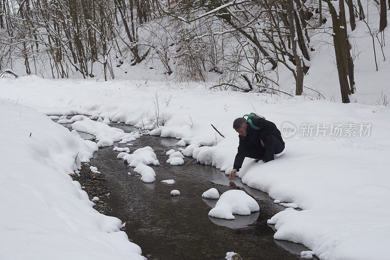 快乐的成年人徒步旅行在下雪的冬天的自然。清凉的冰冻森林溪流。