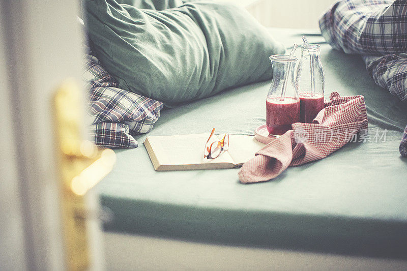 皱巴巴的床上用品与新鲜的粉红色水果冰沙和书一个轻松的一天