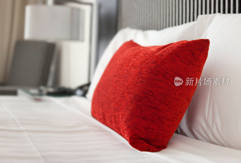酒店床的特写，白色的床单和一个红色的枕头