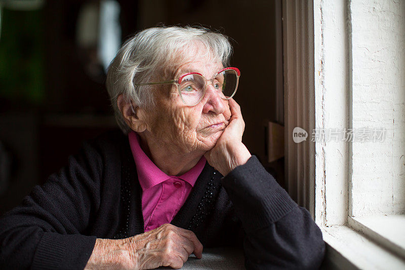 戴眼镜的老妇人若有所思地看着窗外。