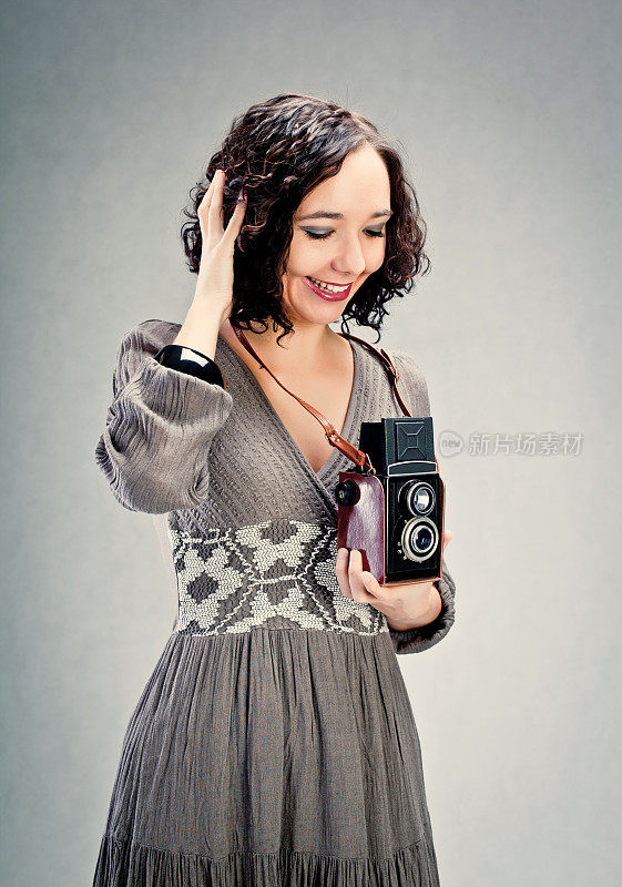 一个兴高采烈的年轻女人，手里拿着一个旧照相机。
