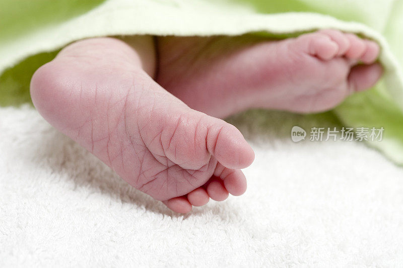 新生婴儿的脚在绿色毯子下