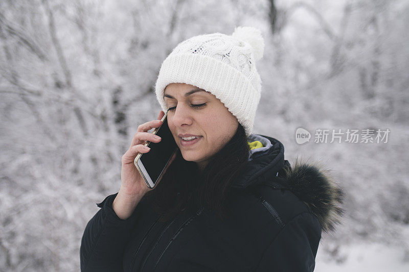 微笑的年轻女子在冬季公园讲手机