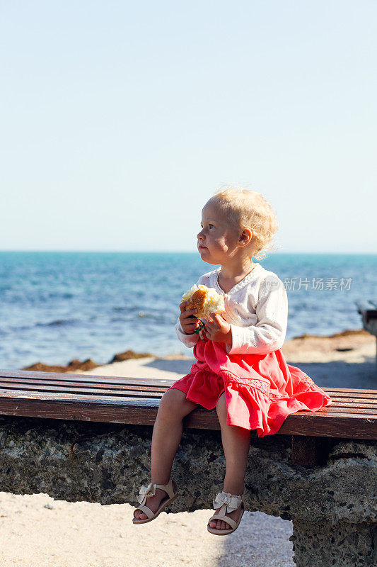 蹒跚学步的小女孩在海滩上吃面包