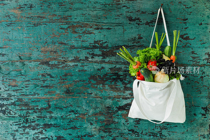 市场新鲜的沙拉蔬菜挂在一个天然棉花可回收的购物袋，用钩子挂在木绿松石色的墙上。