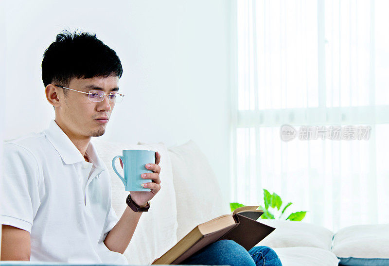 年轻的亚洲人一边喝咖啡一边看书