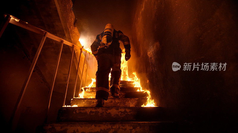 强壮和勇敢的消防员在燃烧的建筑物上楼梯。楼梯被明火燃烧。