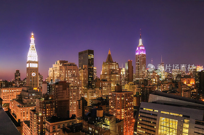 日落时的纽约城市天际线与帝国大厦、大都会人寿保险公司大厦、曼哈顿中城摩天大楼和橙蓝色晴朗的天空。
