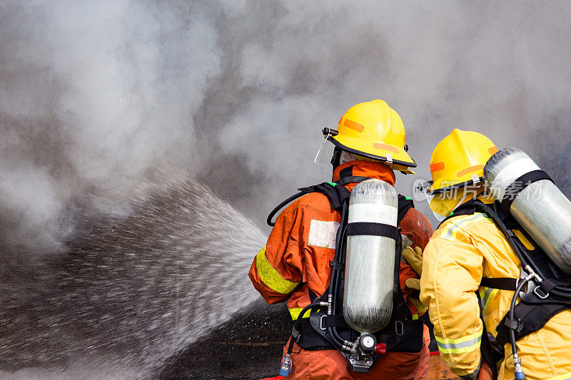 两名消防队员用高压水枪将水喷向火焰周围有烟雾和拷贝空间