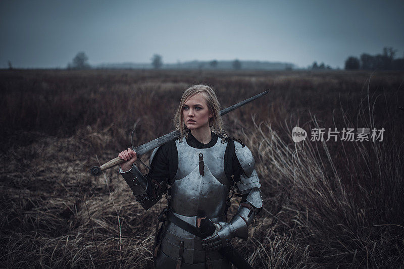 雅娜·达尔克形象中的女孩身穿盔甲，手握利剑，站在草地上。特写镜头。