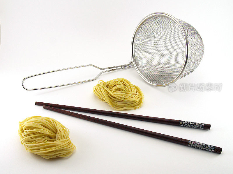 两根黄色的面条，棕色的木筷子和银色金属滤锅孤立在白色的背景上