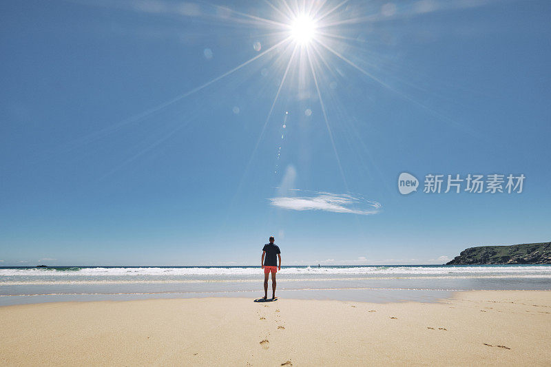 6月一个阳光明媚的炎热日子，一名男子站在康沃尔的佩顿范德海滩的海岸线上。