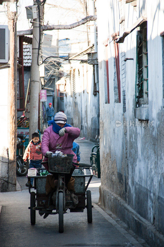 北京胡同里，一位女性骑着三轮车。