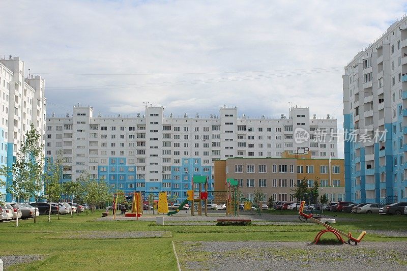 现代宽敞的庭院，明亮的儿童游乐场，停放的汽车和绿色草坪在一个现代化的多层建筑的住宅综合体