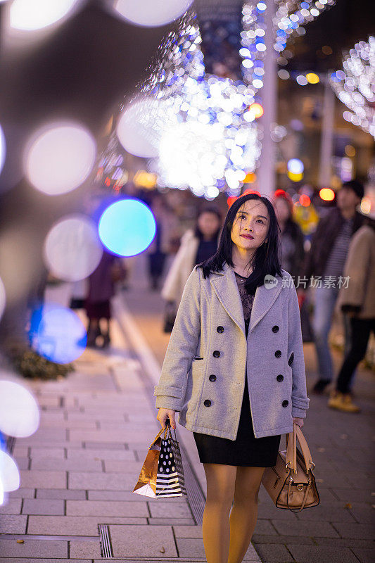 一名亚洲妇女在圣诞之夜走在城市街道上