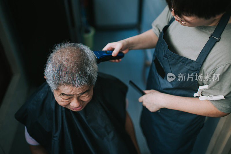 由于旅行禁令，一位亚洲华人中年妇女正在厨房里为她的父亲修剪头发