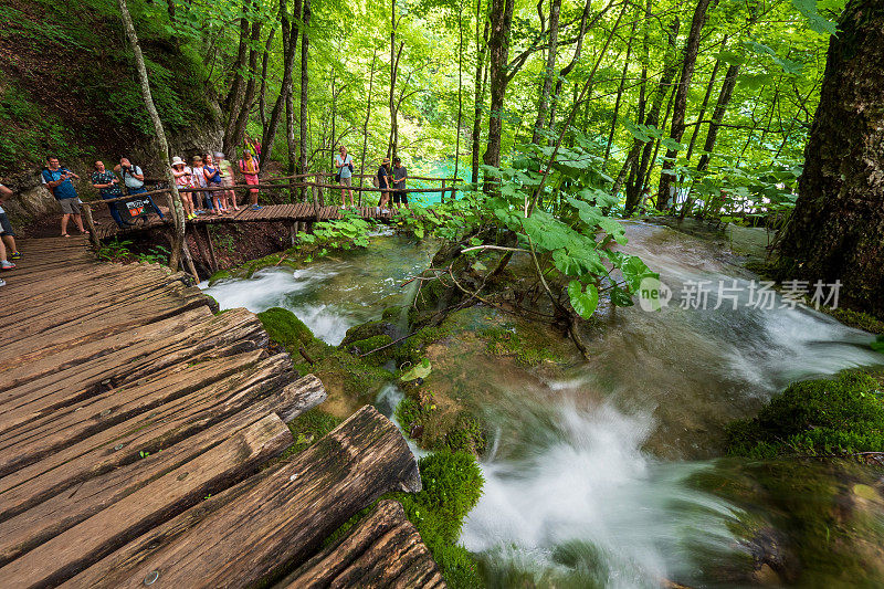 克罗地亚普利特维策湖国家公园，徒步者在木制人行道上散步，经过从岩石上奔流而下的瀑布
