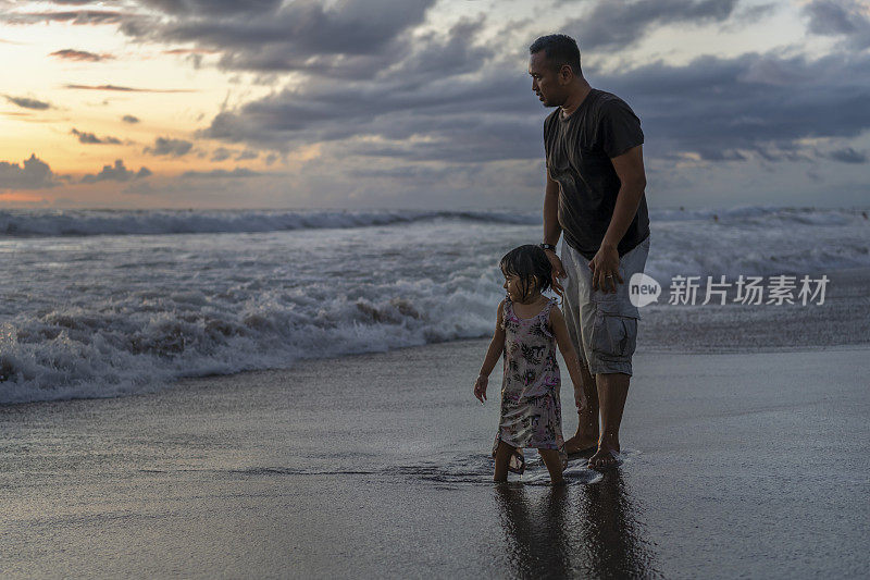 印尼父亲和女儿看在海滩上的撞击声海浪，在日落